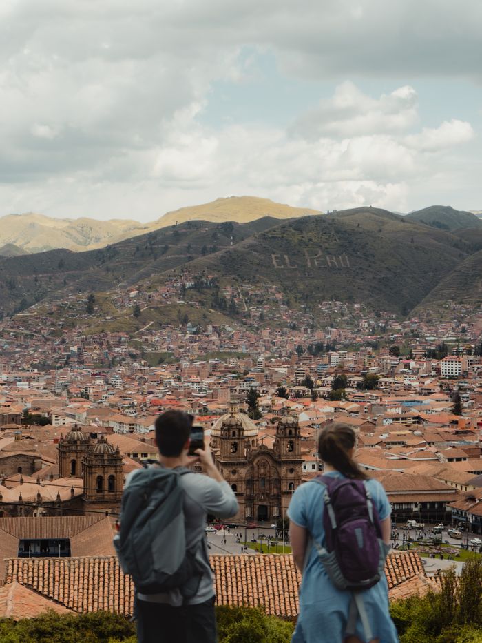 Tourists enjoy a panoramic view of Cusco with mountains and historic architecture.