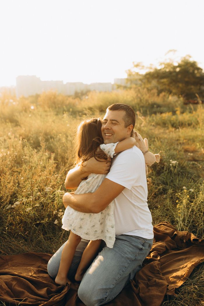 Heartwarming scene of a father and daughter hugging outdoors in a sunny field.