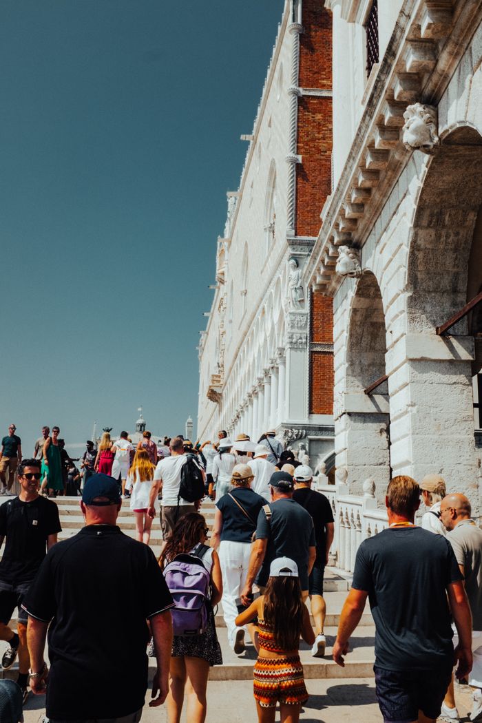 Tourists explore a bustling street beside historic architecture under clear skies.